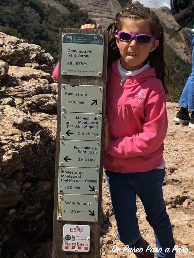 Niña a un lado de poste indicativo de senderos y tiempo estimado de recorrido hasta destino