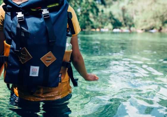 persona dentro de río cristalino con mochila en espalda