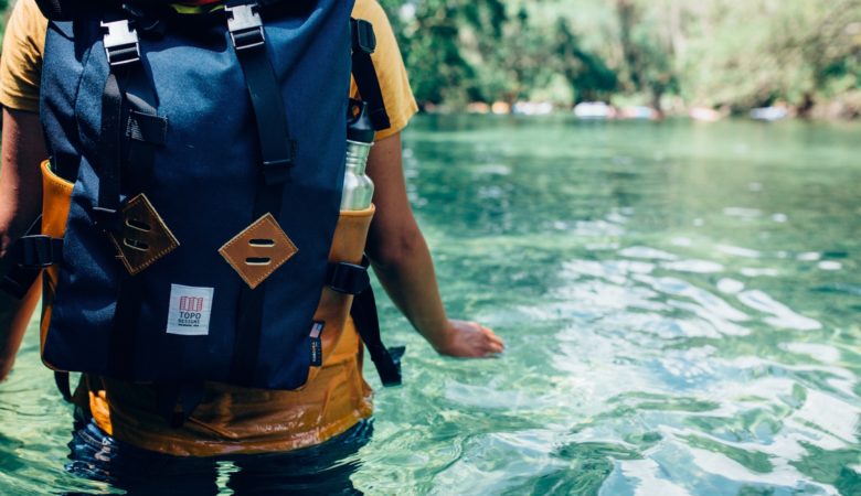 persona dentro de río cristalino con mochila en espalda